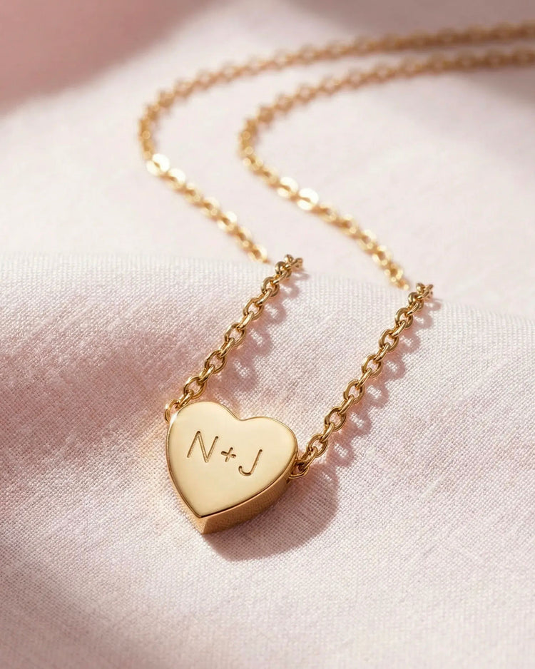 Gold heart-shaped necklace with initials on a pink fabric background