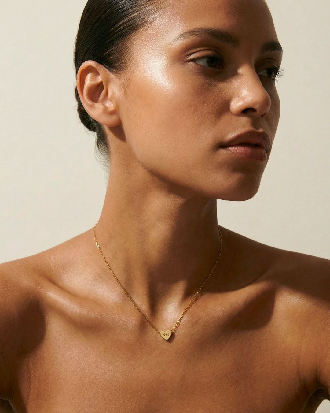 Woman wearing a gold necklace with a heart pendant against a neutral background